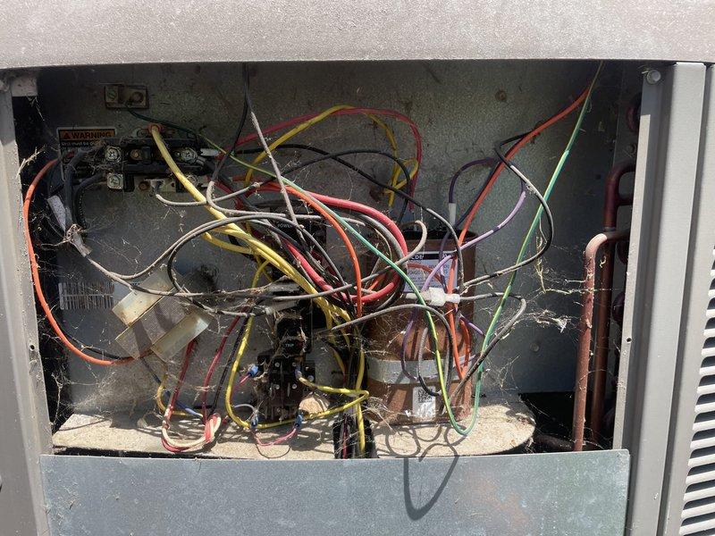 Responded to no-cooling call on 25-year-old residential air conditioning system. Upon arrival, confirmed outside condenser unit was not operating while indoor air handler continued to circulate unconditioned air. Inspected outdoor unit electrical compartment and found heavily soiled components with extensive cobweb accumulation indicating lack of routine maintenance. Tested contactor, capacitor, and compressor functionality. Identified failed dual run capacitor as primary cause of compressor and condenser fan motor failure. Replaced defective capacitor with properly rated component. Cleaned electrical connections and verified proper voltage at all terminals. Cycled system through complete startup sequence and confirmed compressor engaged properly with condenser fan motor operating at correct speed. Measured temperature split at indoor unit showing 18-degree differential, indicating system returned to normal cooling operation. Advised customer of unit's advanced age and recommended cons