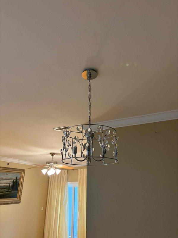 Installed decorative bronze chandelier with crystal accents in residential interior space, featuring cylindrical metal frame with leaf motif details and multiple candelabra-style bulbs. Secured fixture to ceiling mount with chain suspension system, verified proper electrical connections, and confirmed all lighting elements functioning correctly upon completion.
