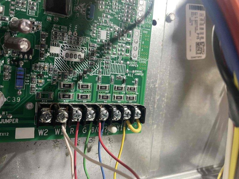 Responded to no cooling call with reported outdoor coil freezing condition on 10+ year old system located next to garage. Upon arrival, system had been off since 8:00 AM per homeowner. Performed diagnostic evaluation of control board and wiring connections, inspecting terminal connections and verifying proper wire placement at W2, W1, R, and G terminals. Documented control board condition and electrical connections with photos showing circuit board components, terminal block wiring, and bundled wire harnesses within control compartment. Advised on freeze-up causes and system status following initial assessment.