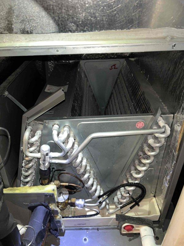 Responded to no cooling complaint with indoor temperature reaching 80 degrees on a 9-year-old air conditioning system. Upon arrival, performed visual inspection of outdoor condenser unit, noting significant dirt and debris accumulation on heat exchanger coil with visible streaking and staining across horizontal fins, which was restricting proper airflow and heat transfer. Inspected indoor evaporator coil assembly in attic space, checking refrigerant line connections, filter drier, condensate drain, and electrical components. Cleaned condenser coil to remove built-up contamination and restore adequate airflow through heat exchanger. Verified proper refrigerant line connections and system operation. System restored to normal cooling capacity following coil cleaning and inspection.
