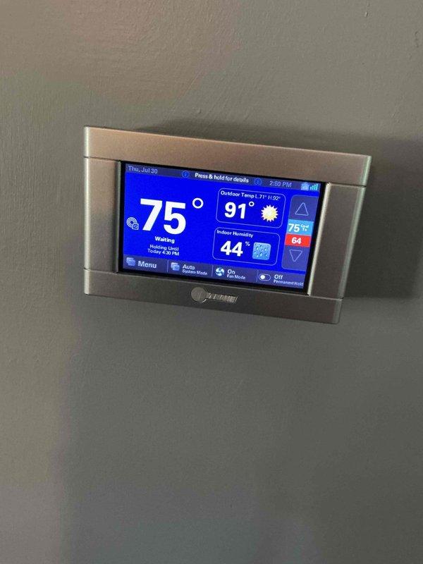 Responded to service call for thermostat displaying two dashes while system continued to cool properly. Upon inspection, found Trane digital thermostat experiencing communication error between display and HVAC system, though cooling operation remained functional. Verified thermostat functionality, cycled power to reset communication protocol, and confirmed proper temperature readings and system response restored with display showing correct indoor/outdoor temperatures and humidity levels.