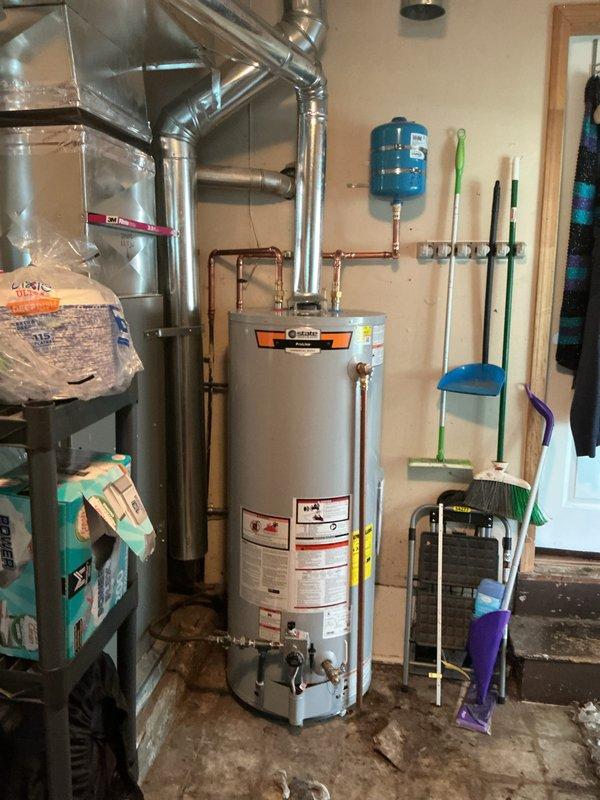Installed a 50-gallon gas tall water heater in residential basement utility room. Connected copper supply lines, gas piping, and venting to existing infrastructure, with blue expansion tank mounted on wall for thermal expansion protection. Installation completed alongside existing HVAC furnace system with all connections properly secured and equipment operational.