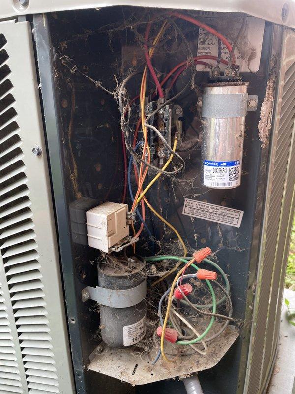 Responded to no cooling complaint on 9-year-old AC system where air handler was running but not producing cool air. Upon inspection, found outdoor condenser unit in poor condition with heavy dirt, dust, and debris accumulation throughout interior compartment, along with aged wiring covered in contaminants. Identified failed dual run capacitor as primary cause of cooling failure, preventing compressor from operating while allowing fan motor to run. Replaced defective capacitor, cleaned electrical connections, and tested system operation. Unit now cooling properly with thermostat displaying 69°F setpoint and system cycling normally.