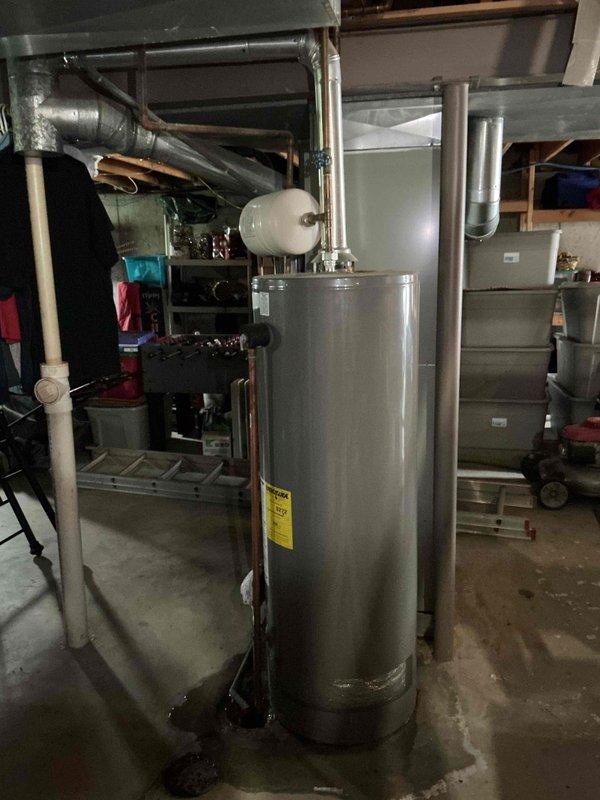 Responded to reported water leak under gas water heater in basement. Completed installation of replacement tanked gas water heater with new expansion tank mounted on top. Connected copper supply lines, installed proper venting with flexible ductwork, and verified all connections for leaks. Unit tested and operational upon completion.