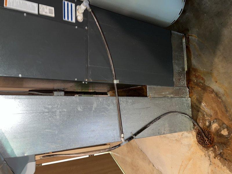 Responded to water leak complaint in basement HVAC system. Upon arrival, inspected air handler unit and surrounding equipment. Found evidence of significant water damage on adjacent wall surfaces with rust-colored staining and vertical streaking patterns indicating prolonged moisture exposure. Examined condensate drain system, water heater connections, and all associated plumbing components connected to the HVAC unit. Documented existing conditions with photographs showing the 10-year-old air handler installation, ductwork, and extent of water damage to concrete walls. Identified source of leak and completed necessary repairs to resolve moisture intrusion issue. System tested and verified operational with no active leaking present at time of departure.