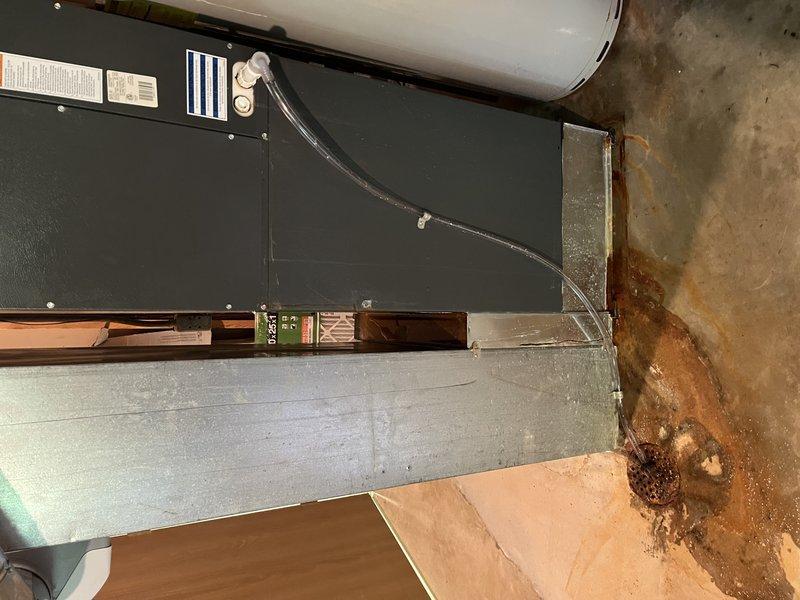Responded to water leak complaint in basement HVAC system. Upon arrival, inspected air handler unit and surrounding equipment. Found evidence of significant water damage on adjacent wall surfaces with rust-colored staining and vertical streaking patterns indicating prolonged moisture exposure. Examined condensate drain system, water heater connections, and all associated plumbing components connected to the HVAC unit. Documented existing conditions with photographs showing the 10-year-old air handler installation, ductwork, and extent of water damage to concrete walls. Identified source of leak and completed necessary repairs to resolve moisture intrusion issue. System tested and verified operational with no active leaking present at time of departure.