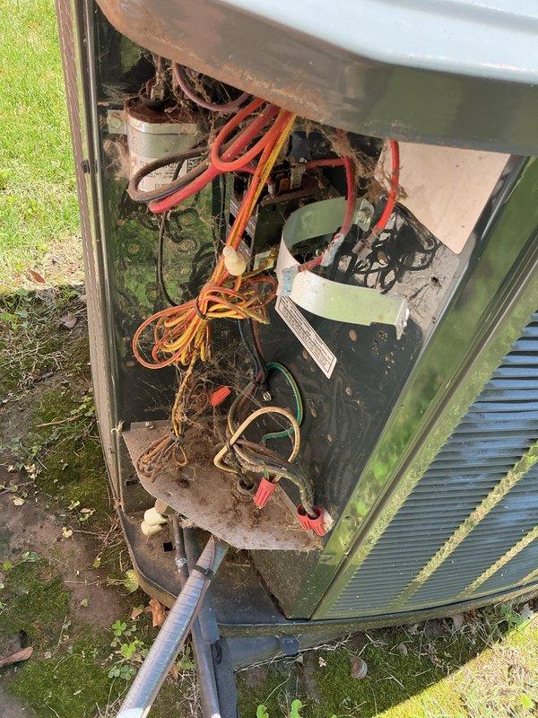 Responded to no cooling complaint on 10+ year old outdoor condenser unit. Upon arrival, found system blowing warm air with indoor temperature at 84 degrees. Performed diagnostic evaluation of outdoor unit located on ground-level concrete pad at side of residence. Opened access panel and inspected internal components, noting extensive rust and corrosion throughout metal framework and base, accumulated debris in compartment, and aged electrical connections. Observed deteriorated condition of capacitor and wiring. Unit exhibited significant weathering consistent with age and outdoor exposure. Documented system condition with photographs showing corroded interior components and overall exterior cabinet condition. Recommended necessary repairs to restore cooling operation.