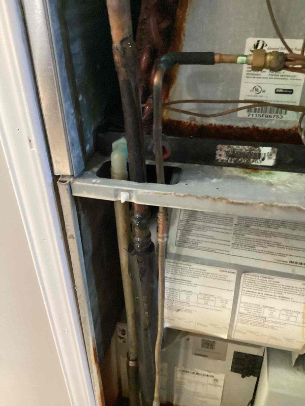 Responded to callback for water pooling around indoor air handler unit in basement. Upon inspection, found significant condensation on evaporator coil with water accumulation at base of unit. Identified excessive sweating on coil surfaces and surrounding components, with visible corrosion and rust staining on metal surfaces and copper refrigerant lines. Documented equipment condition showing advanced deterioration on cabinet panels, pipe connections, and mounting brackets. Investigation revealed drainage issue causing moisture buildup around air handler. Photographed serial number 7115F06753 and overall equipment condition for service records.