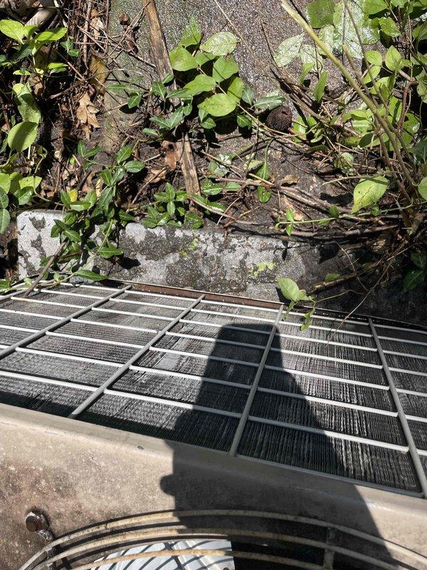 Completed preventive maintenance tune-up on outdoor HVAC unit. Inspected condenser coil and filter assembly, noting accumulated dirt and debris on mesh filters requiring attention. Observed vegetation overgrowth around unit perimeter and dust accumulation on equipment surfaces and refrigerant lines, documented conditions with photos for service records.