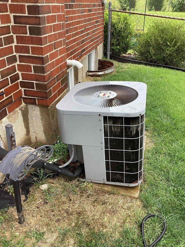 Completed cooling system tune-up on residential air conditioning unit located in side yard. Unit is over 10 years old and positioned on concrete pad adjacent to structure. Performed standard preventive maintenance protocol including inspection of condenser coils, fan operation, and refrigerant levels. Documented equipment condition with photographs showing AC unit with light gray casing and black protective grille in serviceable condition with adequate clearance around unit for proper airflow. System operational upon completion of tune-up service.