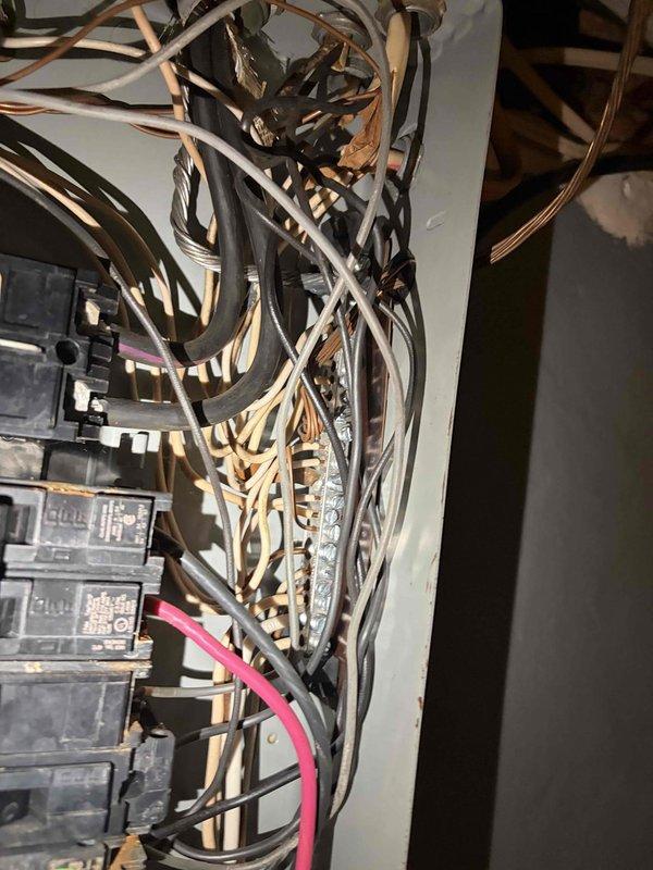 Conducted comprehensive assessment of existing 100-amp electrical panel and meter assembly for replacement estimate. Documented current panel configuration showing multiple circuit breakers with extensive wiring in various colors, copper conduit entries from ceiling joists, and visible signs of aging including rust and corrosion at panel base. Evaluated wire routing, breaker arrangement, conduit connections, and overall system condition to determine scope of work required for complete panel and meter upgrade.