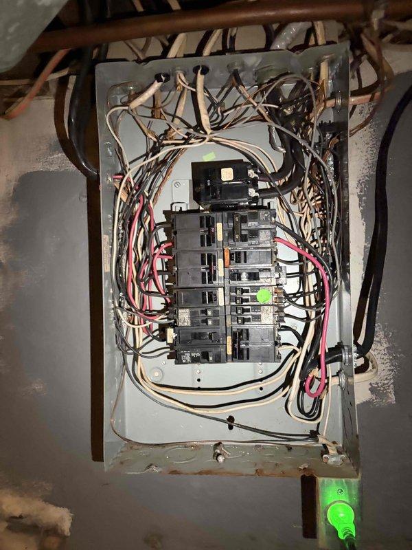 Conducted comprehensive assessment of existing 100-amp electrical panel and meter assembly for replacement estimate. Documented current panel configuration showing multiple circuit breakers with extensive wiring in various colors, copper conduit entries from ceiling joists, and visible signs of aging including rust and corrosion at panel base. Evaluated wire routing, breaker arrangement, conduit connections, and overall system condition to determine scope of work required for complete panel and meter upgrade.