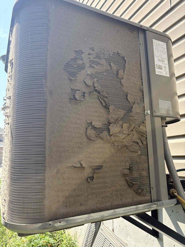 Responded to no cooling call on residential HVAC unit less than 10 years old located in side yard. Upon arrival, found outdoor condenser unit with severe deterioration of protective outer covering and insulation material, with large sections peeled away exposing the underlying coil fins. Documented equipment condition with photos showing extensive surface damage to unit housing while metal heat exchanger fins remained relatively intact. Advised customer that unit had been turned off per prior instructions due to warm air discharge from system.