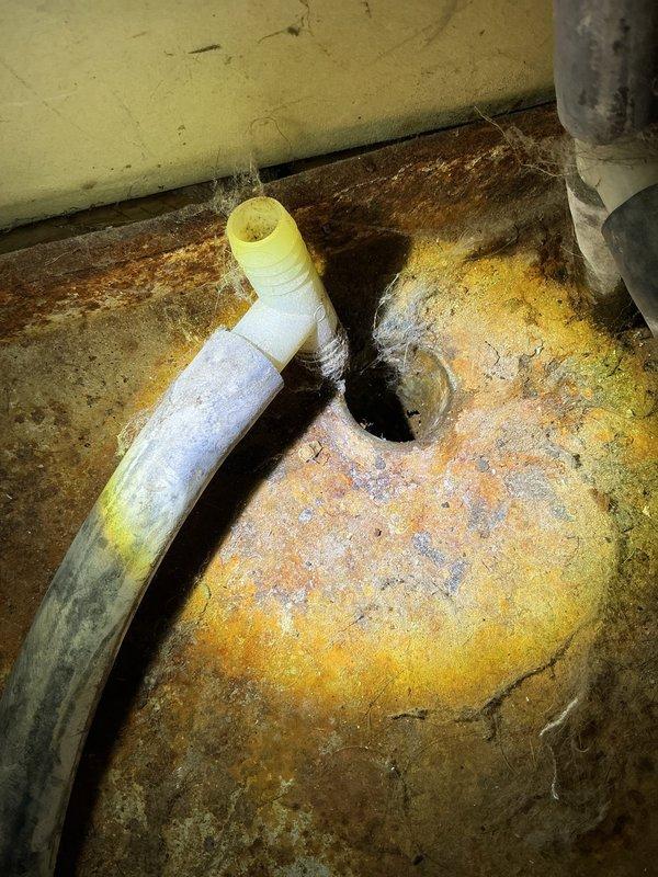 Responded to emergency call for second-floor air conditioning unit experiencing active water leakage. Upon arrival, located air handler in second-floor utility closet with evidence of condensate drainage issues. Inspection revealed severely stained and discolored condensate drain line with significant mineral deposits and buildup around floor penetration point. Concrete floor exhibited extensive water damage and staining patterns indicating prolonged drainage problems. Advised homeowner to shut down system and operate in fan-only mode to prevent further water damage until repairs could be completed. Documented conditions with photographic evidence showing HVAC equipment location and drain line deterioration for repair estimates.