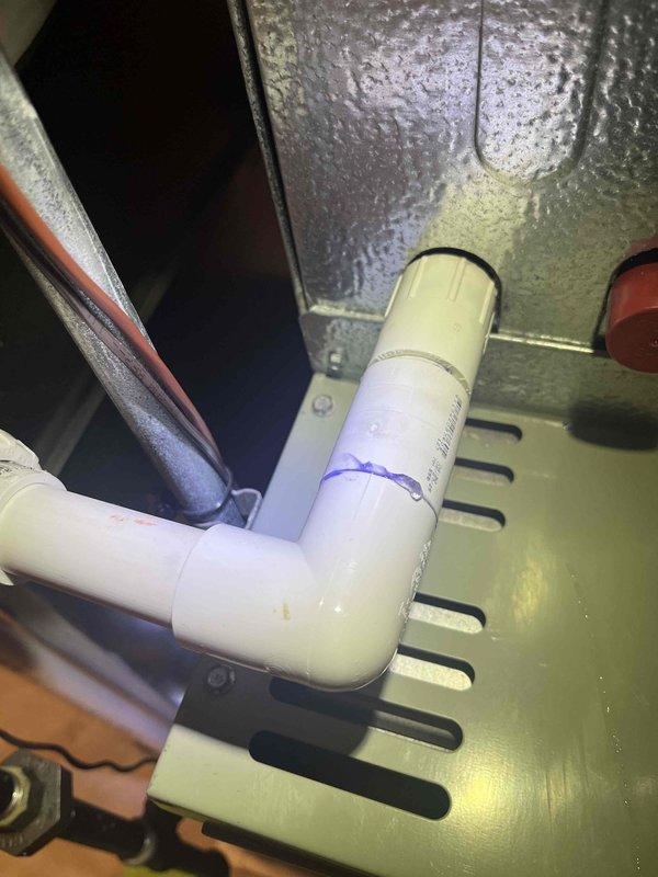 Responded to callback for water leakage on 12-year-old Trane air conditioning unit that was recently serviced. Inspected condensate drain system and drain pan assembly, documenting PVC drain line configuration and pan condition with photos. System shows signs of ongoing drainage issues requiring further evaluation of condensate removal components.