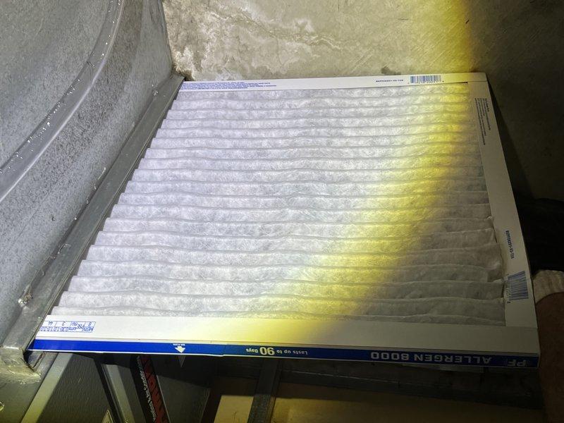 Responded to no-cooling call and found water leaking from bottom of furnace unit. Upon arrival, discovered significant water damage on concrete floor surrounding equipment, with extensive staining and moisture saturation indicating ongoing leak. Inspected HVAC system and identified heavily contaminated air filter with substantial dirt and particulate buildup affecting approximately one-third of filter surface. Advised customer that unit had been properly shut off per instructions to prevent further water damage. Documented conditions with photographs showing water heater installation area, floor damage patterns, and compromised filter condition. Recommended immediate repair of leak source and filter replacement to restore proper system operation.