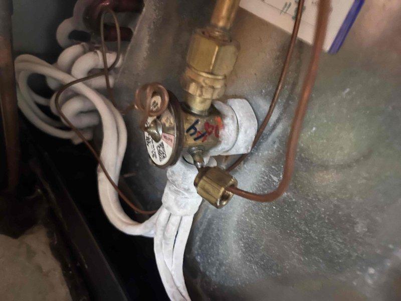Responded to no cooling complaint on ground-level hallway unit. Upon arrival, connected manifold gauge set to outdoor condenser unit to assess refrigerant pressures and system performance. Diagnosed system issue and advised customer to shut off air conditioning system immediately to prevent further damage while leaving fan in run mode to maintain air circulation. Inspected indoor components including what appears to be the air handler or associated equipment with pressure relief valve and copper refrigerant lines showing age-related oxidation on brass fittings.