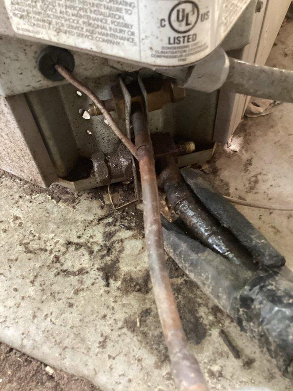 Performed complimentary second opinion inspection on air conditioning system to evaluate reported refrigerant leak. Upon examination of the refrigerant line connections, identified missing service port caps on multiple Schrader valve fittings, which can allow refrigerant loss and contamination entry into the system. Documented conditions with photos showing corroded copper tubing, aging valve assemblies, and exposed service ports requiring proper sealing to maintain system integrity.