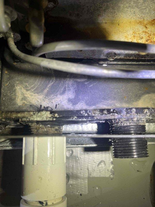 Responded to callback for AC unit leaking at evaporator coil drain in basement. Inspected 10-year-old system and identified condensate drain line issue with visible corrosion and mineral buildup on drainage components. Cleared blockage in drain line, verified proper condensate flow, and confirmed leak resolution at A-coil drain assembly.