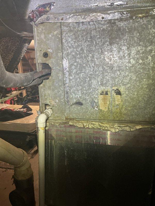Responded to no cooling complaint with reported frozen refrigerant line. Upon arrival, conducted system inspection of aged HVAC unit in basement utility area. Examined air handler cabinet showing significant wear and mineral deposits, inspected supply register and ductwork connections. Documented equipment condition with photographic evidence showing weathered exterior surfaces, PVC condensate drain line, and ventilation components for diagnostic purposes and potential follow-up recommendations.