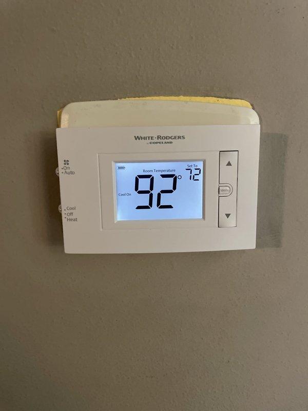 Responded to service call for non-functional thermostat in upstairs hallway. Upon arrival, found existing Emerson thermostat with inoperative display and unresponsive buttons, showing signs of age and wear with discoloration. Replaced failed unit with new White-Rodgers programmable thermostat. Verified proper system operation with cooling mode activated, display functioning correctly showing room temperature of 92 degrees and setpoint of 72 degrees. System tested and confirmed operational.
