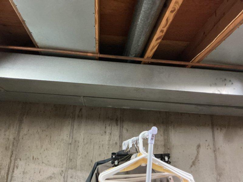 Responded to report of water dripping into lower level bedroom. Upon inspection, accessed ceiling cavity and identified water staining on wooden joists and structural members. Created access opening in ceiling to investigate source of moisture intrusion. Documented conditions with photos showing discoloration on framing members and concrete foundation walls, indicating active or recent water infiltration from above living space.