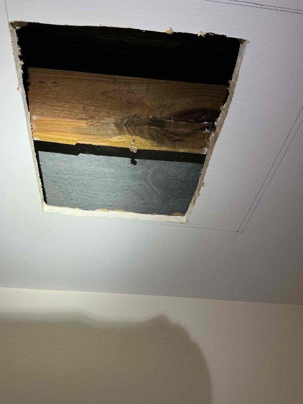 Responded to report of water dripping into lower level bedroom. Upon inspection, accessed ceiling cavity and identified water staining on wooden joists and structural members. Created access opening in ceiling to investigate source of moisture intrusion. Documented conditions with photos showing discoloration on framing members and concrete foundation walls, indicating active or recent water infiltration from above living space.