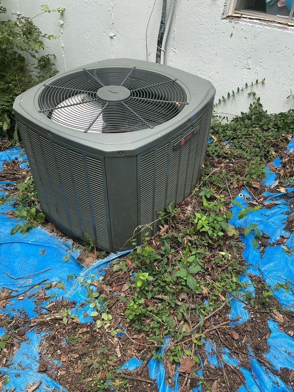 Responded to no cooling complaint on outdoor condensing unit located on side of home. Upon arrival, found unit experiencing airflow restriction due to excessive vegetation growth and debris accumulation around condenser coil fins. Cleared weeds, vines, and organic matter from unit perimeter and removed leaves and plant debris from top grille and surrounding area. Inspected condenser coil and verified airflow obstruction was impeding heat exchange efficiency. Unit tested and confirmed restored to proper cooling operation after clearing vegetation and debris.
