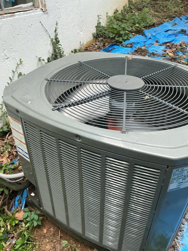 Responded to no cooling complaint on outdoor condensing unit located on side of home. Upon arrival, found unit experiencing airflow restriction due to excessive vegetation growth and debris accumulation around condenser coil fins. Cleared weeds, vines, and organic matter from unit perimeter and removed leaves and plant debris from top grille and surrounding area. Inspected condenser coil and verified airflow obstruction was impeding heat exchange efficiency. Unit tested and confirmed restored to proper cooling operation after clearing vegetation and debris.