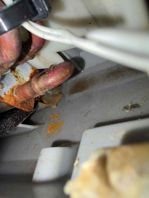 Responded to callback for AC unit cooling only one room in residence with system under 10 years old located in bedroom. Upon inspection, discovered severely corroded copper refrigerant line connections with heavy oxidation and deterioration at joints. Identified compromised condensate drain line connections at exterior foundation with visible moisture accumulation and improper drainage. Corrosion patterns indicated prolonged exposure to moisture and possible refrigerant leak at connection points. Documented condition of affected components with photographic evidence showing extent of copper pipe deterioration and drain line issues. System requires refrigerant line replacement and condensate drain repair to restore proper operation and prevent further damage.