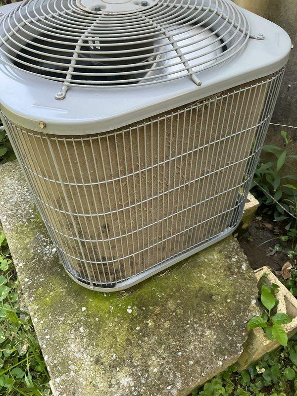 Responded to no cooling call on residential outdoor condensing unit less than 10 years old located in backyard. Upon arrival, found system not operating. Performed diagnostic inspection of condenser unit, which showed signs of outdoor weathering and vegetation growth around base and concrete pad. Documented equipment condition with photos showing wire mesh protective cage, cooling fins with accumulated dirt and discoloration, and surrounding plant growth encroaching on unit. Completed system evaluation and contacted owner for authorization to proceed with necessary repairs to restore cooling operation.