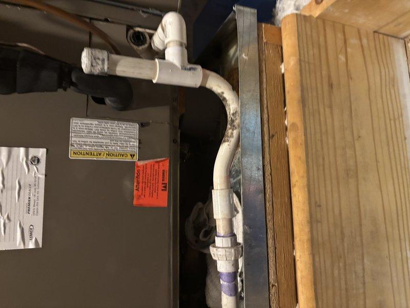 Responded to reported AC system leak in attic location. Upon inspection, identified active water leak originating from the condensate drainage system on HVAC unit less than 10 years old. Examined PVC condensate line configuration and connections for blockages or improper drainage. Documented equipment condition and leak source with photographic evidence showing condensate piping assembly and affected interior areas including ceiling and crown molding where water intrusion was visible. Provided assessment and repair recommendations to resolve drainage issue and prevent further water damage.