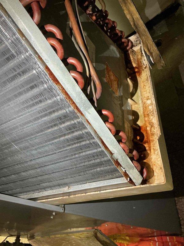 Responded to reported water leak from basement furnace unit over 10 years old. Upon inspection, identified significant rust staining and corrosion on furnace cabinet panel and evaporator coil assembly, indicating chronic moisture exposure. Documented extensive rust deposits on heat exchanger fins, refrigerant line connections, and metal housing components. Photographed affected areas showing corrosion patterns originating from mounting points and spreading across cabinet surfaces, as well as deterioration along coil edges and copper refrigerant lines.