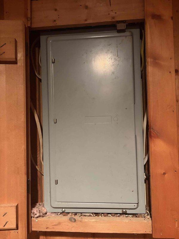 Completed comprehensive Elite electrical inspection of residential service panel and distribution system. Documented existing main breaker panel installation in wooden-framed utility area, noting standard gray metal enclosure with hinged door and secure latch mechanism. Inspected interior circuit breaker configuration revealing multiple branch circuits with mixed breaker types including standard single-pole and multi-pole devices. Observed existing circuit identification system with handwritten labels and documentation posted adjacent to panel for reference. Verified panel accessibility and noted presence of service documentation including circuit schedules affixed to surrounding wall structure. Assessed overall panel condition, identifying normal operational wear and minor surface soiling consistent with typical residential use. Photographed panel exterior and interior arrangements for maintenance records, capturing current breaker positions, labeling system, and general installation 