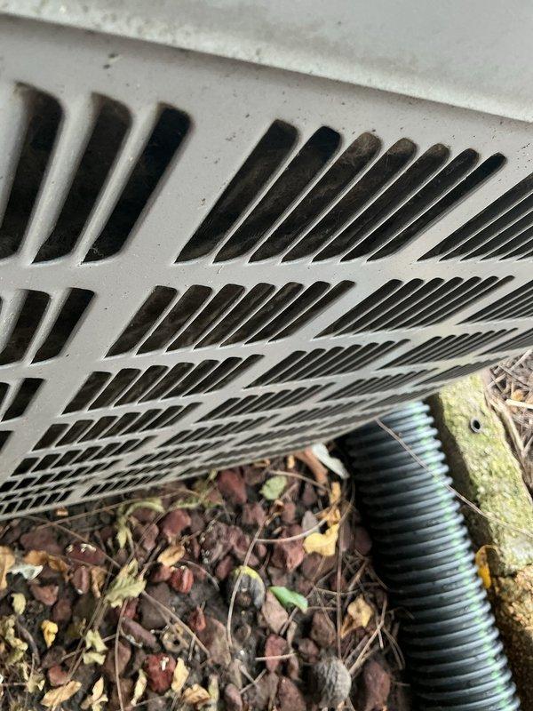 Responded to no cooling complaint on 10+ year old outdoor AC unit. Upon arrival, confirmed unit was blowing warm air with rising indoor temperatures. Inspected exterior condensing unit located at side of home and identified blocked foundation ventilation grates restricting proper airflow to equipment. Removed accumulated debris, leaves, mulch, and organic matter from vent openings and surrounding area. Cleared drainage hose obstruction and restored adequate ventilation clearance around unit foundation. Verified airflow restoration and advised on maintaining clear perimeter for optimal system performance.