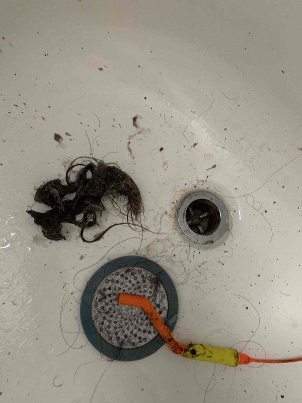 Responded to service call for multiple plumbing issues including shower and sink drain blockages, malfunctioning outdoor spigots, and hissing toilet. Successfully cleared shower drain obstruction by removing accumulated hair and organic debris using drain snake and manual extraction methods. Disassembled and cleaned drain assembly, including perforated strainer and rubber gasket components. Inspected toilet tank mechanism and identified source of hissing noise related to fill valve operation. Evaluated front and rear exterior hose bibs; rear spigot handle turned but failed to deliver water flow, indicating internal stem or seat failure requiring repair. Documented all findings with photographic evidence showing extracted drain debris, exposed drain components with plumbing tools in place, and interior toilet tank mechanisms including flush valve, fill valve with float assembly, and connecting hardware. All accessible drain clearing work completed; additional repairs recommended for non