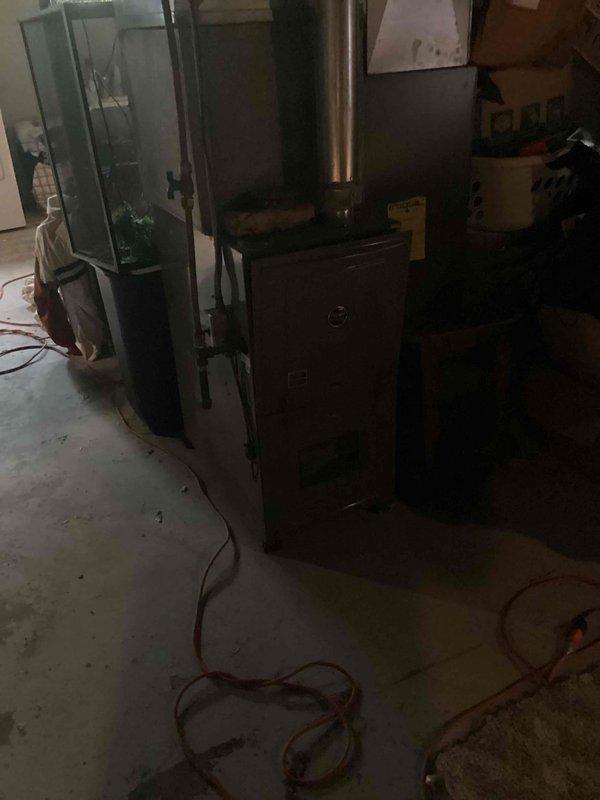 Responded to no-cool emergency call for residence with small children and indoor temperature at 90 degrees. Upon arrival, found 10+ year old ground-level unit blowing warm air with active water leak. Confirmed system had been turned off per prior instructions with fan left in circulation mode. Performed diagnostic evaluation of both indoor air handler and outdoor condensing unit. Identified refrigerant leak causing loss of cooling capacity and resulting condensate drainage issue. Documented thermostat reading of 80 degrees at time of service and captured equipment condition photos showing furnace, air handler assembly, refrigerant lines, and overall installation in basement mechanical room.