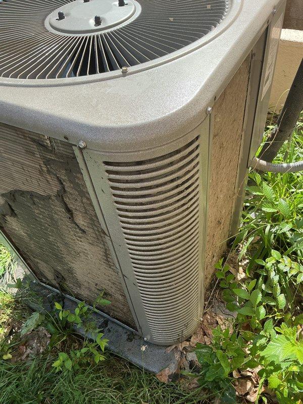 Responded to service call for AC unit not cooling at residential property. Upon arrival, performed visual inspection of outdoor condenser unit, which showed signs of weathering and environmental exposure consistent with 10-year-old equipment. Documented unit condition with photographs showing significant dirt accumulation on cabinet surfaces, water staining on side panels, and overgrown vegetation around base restricting proper airflow. Cleared debris and vegetation from around unit perimeter to restore adequate clearance for ventilation. Inspected condenser coils through louvers and noted moderate dirt buildup affecting heat transfer efficiency. System operational assessment and diagnostic testing completed to identify cooling deficiency cause.