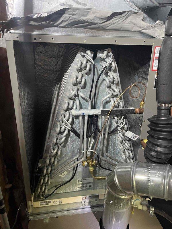 Continued leak search on residential AC system under first-year warranty that was not cooling. Connected refrigerant manifold gauges to measure system pressures and temperatures, recording readings of 533.3 PSIG suction and 540.4 PSIG discharge with corresponding temperatures. Inspected evaporator coil assembly which showed heavy dust and debris accumulation on A-frame coil surfaces that could restrict airflow and reduce cooling capacity. Previous service visit was interrupted due to weather conditions; completed diagnostic testing during this follow-up to identify source of cooling issue and potential refrigerant leak.