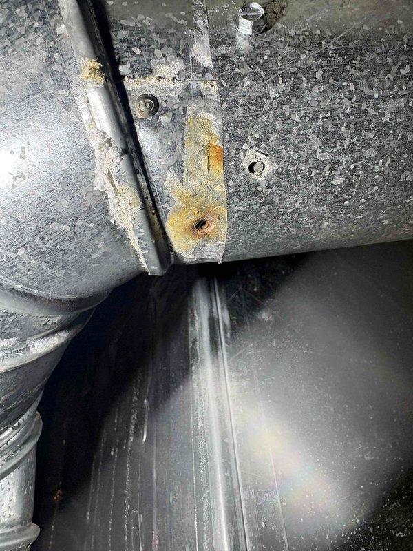 Responded to service call for AC unit leaking in basement. Upon inspection, discovered significant moisture accumulation on ductwork and evidence of condensation issues in confined mechanical space. Identified rust and corrosion on metal brackets and mounting hardware, along with visible water staining on insulation materials. Documented existing conditions of 10-year-old outdoor unit and associated ductwork system showing signs of age-related deterioration. Photographed affected areas including compromised insulation, condensation on reflective duct surfaces, and corroded fastening components for repair recommendations.