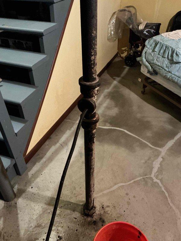 Responded to kitchen sink clog on main living level. Upon arrival, discovered the drainage issue was related to severely corroded vertical plumbing stack visible in lower level beneath kitchen. The deteriorated metal pipe showed extensive rust and corrosion throughout, with active water leakage at base requiring bucket placement for containment. Assessed pipe condition and cleared obstruction in drainage system to restore proper flow. Documented extensive corrosion damage to vertical stack for future repair recommendations, as pipe replacement will be necessary to prevent continued leakage and potential water damage to surrounding areas.