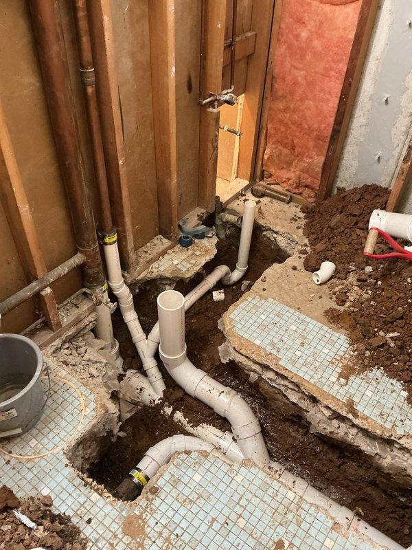 Completed plumbing permit 26-001638 involving the removal and replacement of existing cast iron drain piping with new PVC drainage system. Excavated concrete floor and trenched to access underground piping, then installed new white PVC drain lines to accommodate relocated tub drain for new shower base installation. Installed new shower valve assembly with copper supply lines run vertically through wall framing. All new piping was properly fitted, connected, and positioned according to code requirements to support the updated bathroom fixture layout.