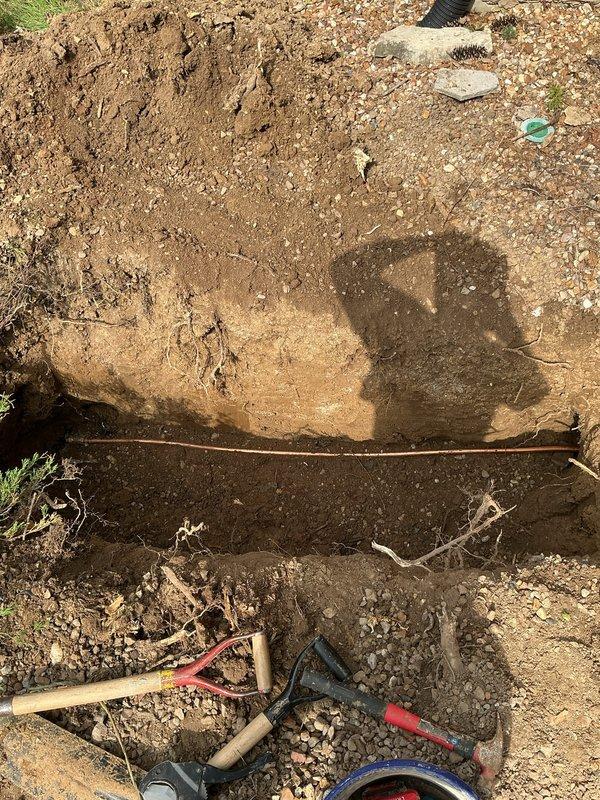 Responded to emergency water service repair requiring both interior and exterior excavation work. Accessed existing copper water service line through interior wall, exposing copper piping with brass fittings and elbow connections near structural floor joists. Excavated exterior trench to locate and repair underground water service line, removing soil layers to access damaged section. Completed necessary repairs to restore water service functionality and backfilled excavation upon completion.