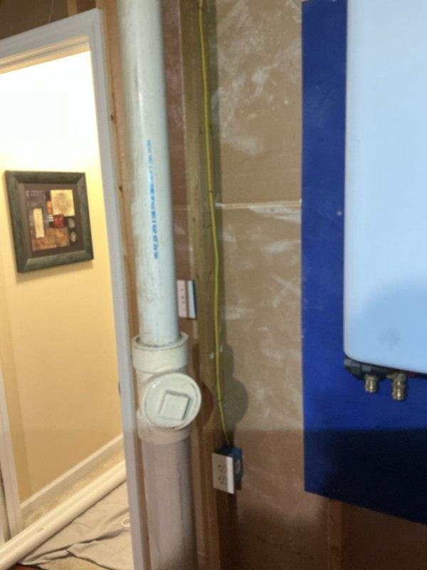 Completed installation of tankless water heater unit in basement utility area with exposed framing. Unit mounted to wall studs with proper venting and drainage connections established using white PVC piping, including cleanout access point for future maintenance. All electrical connections completed in accordance with code requirements, utilizing existing electrical infrastructure and panel access.
