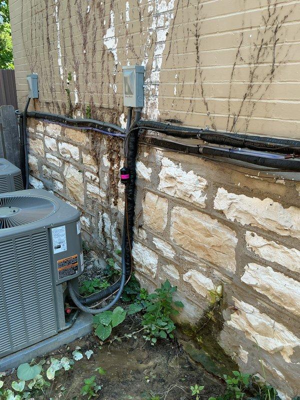 Responded to callback for water pooling around 3-month-old Lennox system. Upon arrival, inspected outdoor condensing unit and surrounding area for source of water accumulation. Examined condensate drain line routing, primary and secondary drain connections, and evaporator coil drain pan for proper installation and function. Verified refrigerant lines, electrical conduit, and all exterior connections were properly sealed and secured to building exterior. Documented site conditions with photographs showing unit placement, wall-mounted components, and ground-level drainage patterns. System operational at time of inspection with no active leaks observed during service visit.