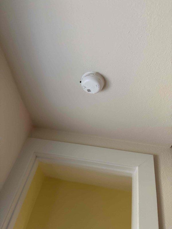 Completed installation of smoke detectors and electrical outlets per approved estimate. Mounted circular smoke detector on ceiling above doorway with proper positioning for optimal detection coverage. Installed standard duplex receptacle with indicator light on wall near ceiling junction. All electrical connections secured and tested for proper operation.