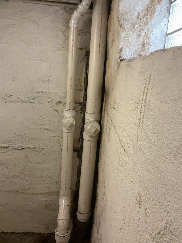 Installed new white PVC drainage piping system in basement utility area, running vertical waste lines along masonry wall with proper fittings and cleanout access points. All pipes were securely mounted and connected with elbow joints for directional transitions, ensuring proper drainage flow in accordance with plumbing code requirements.
