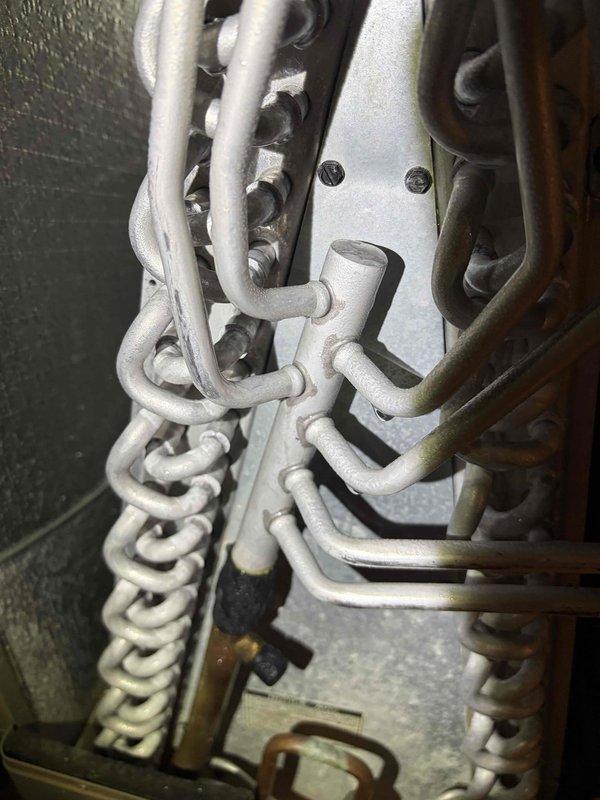 Responded to report of HVAC equipment leaking. Upon inspection, documented the condition of the unit's internal components, including the heat exchanger assembly, evaporator coil section, and associated mechanical linkages. Photographed the chain-driven mechanism and internal cabinet components showing the U-bend heat exchanger tubes, insulated refrigerant lines, and burner assembly to assess the source of the reported leak and determine necessary repairs.