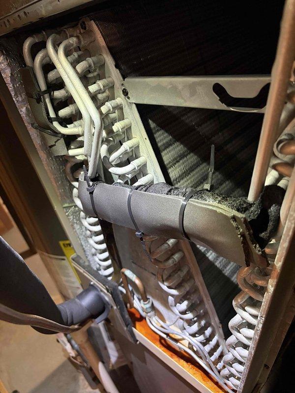 Responded to report of HVAC equipment leaking. Upon inspection, documented the condition of the unit's internal components, including the heat exchanger assembly, evaporator coil section, and associated mechanical linkages. Photographed the chain-driven mechanism and internal cabinet components showing the U-bend heat exchanger tubes, insulated refrigerant lines, and burner assembly to assess the source of the reported leak and determine necessary repairs.