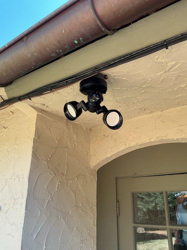 Replaced failed exterior motion detector light fixture at driveway location with customer-supplied dual-head security light. Removed existing 12-year-old single fixture, verified electrical connections, and installed new motion-sensor lighting unit on textured stucco wall beneath eave and gutter system. All wiring connections secured and fixture tested for proper operation.
